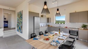 A modern kitchen with a dining area, featuring a large island, stainless steel appliances, and pendant lighting.