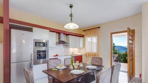 Una cucina moderna con elettrodomestici in acciaio inossidabile, un'area pranzo con tavolo e sedie in legno e vista sull'esterno.