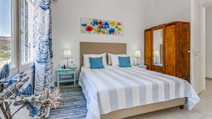Quarto com cama, mesas de cabeceira, espelho e janela com cortinas.