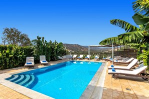 Una piscina rectangular d'aigua blava i cristal·lina, envoltada de gandules i una pèrgola amb fulles de plàtan.