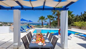 A dining area with a pool view, outdoor seating, and a clear sky. - Villa Almyrida View by Villa Plus (Apokoronos)