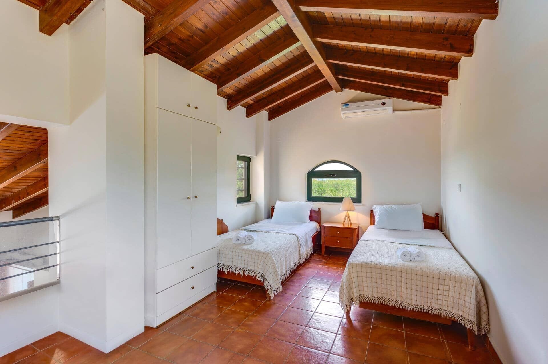 Una habitación con dos camas, techo de madera, una ventana y un armario blanco.