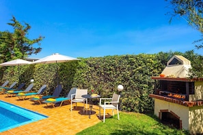 A pool area with lounge chairs, a table, and a barbecue grill.