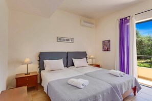 A bedroom with a bed, two bedside tables, a nightstand, a window with purple curtains, and a picture on the wall.