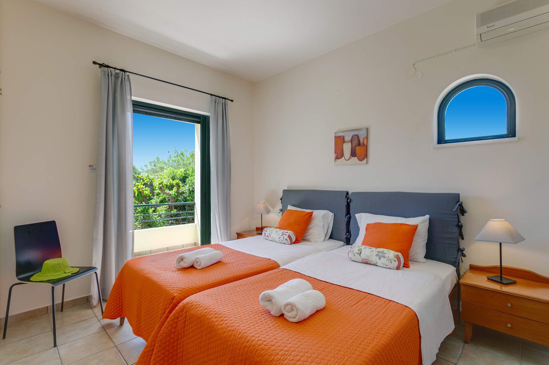 Ein Hotelzimmer mit zwei Betten, einem Balkon, einem Sessel und einem Schreibtisch.