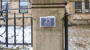 Um pilar de pedra com uma placa que diz "25 Eden House Apartments" em frente a um edifício com janelas em arco.