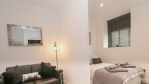 Quarto moderno com cama, mesa de centro de vidro, sofá e abajur.