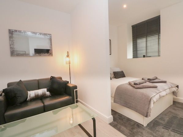 A modern bedroom with a bed, a glass coffee table, a sofa, and a floor lamp.