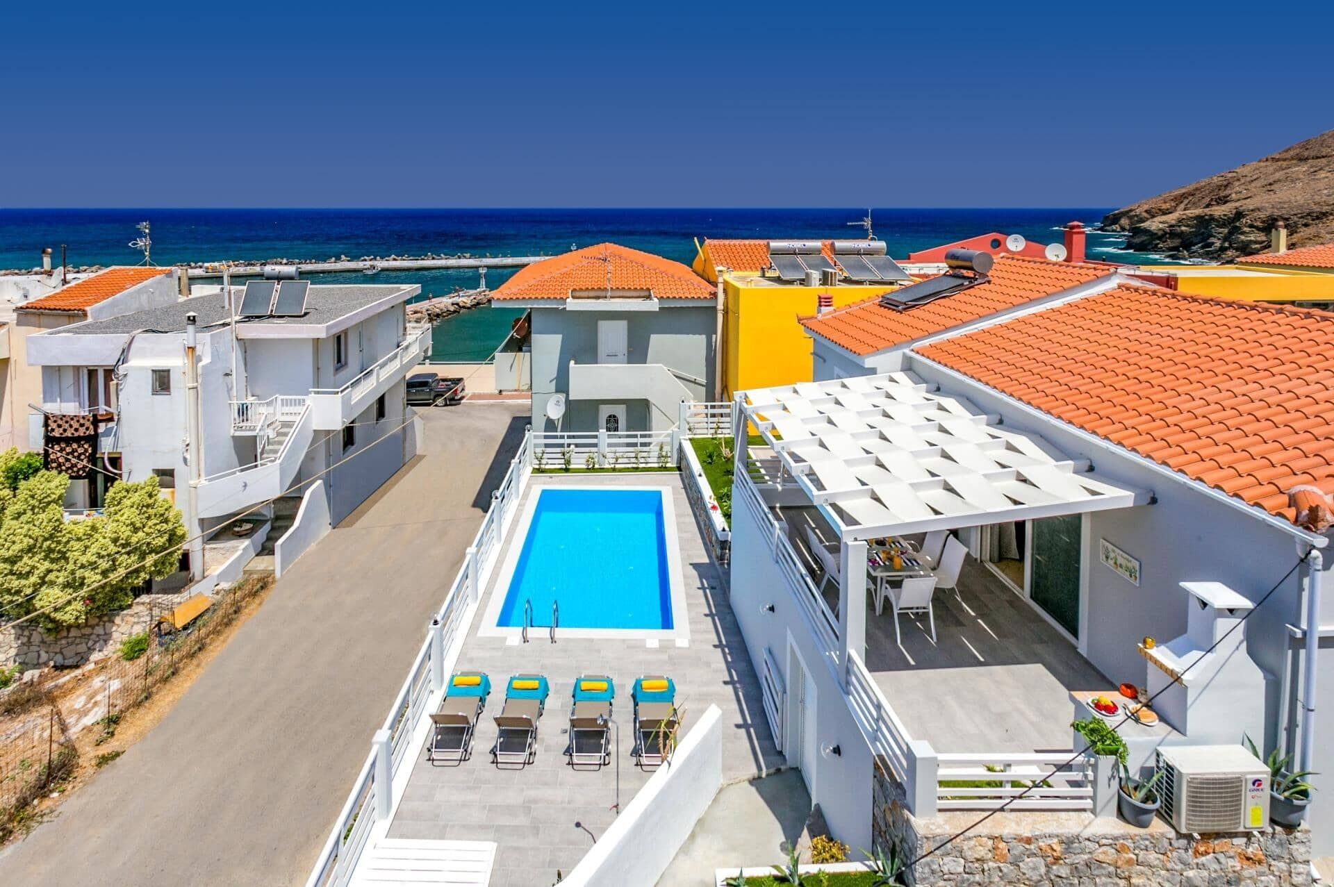 A rooftop pool with sun loungers, a clear view of the sea, and a mix of modern and traditional architecture.