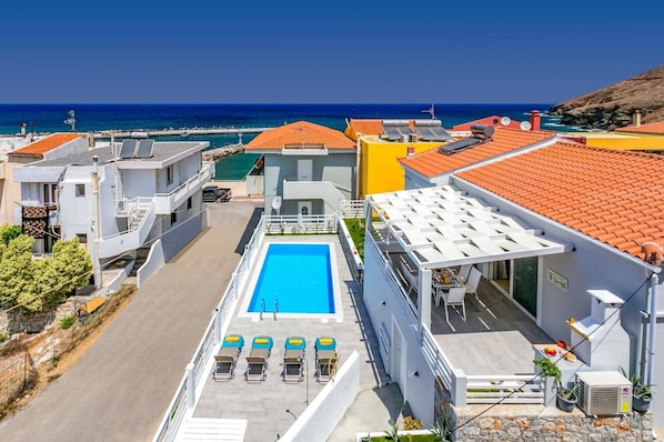 A rooftop pool with sun loungers, a clear view of the sea, and a mix of modern and traditional architecture.