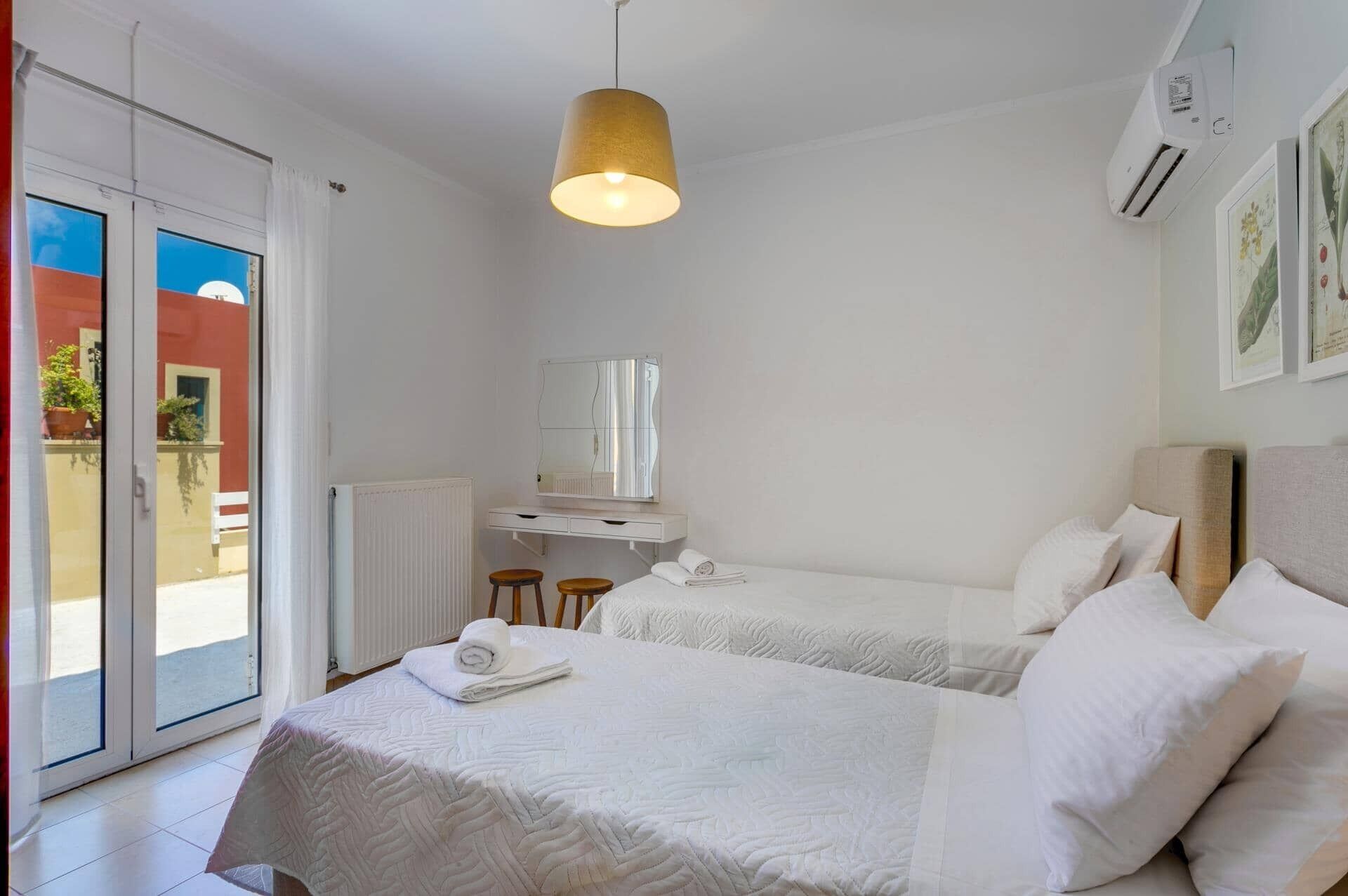 Une chambre d’hôtel avec deux lits, une grande fenêtre, un radiateur et un luminaire au plafond.