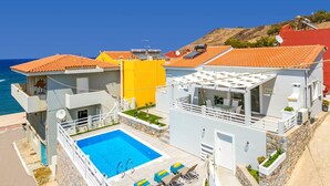 A coastal hotel with a swimming pool, outdoor seating, and a view of the sea. - Villa Areva by Villa Plus (Panormos)