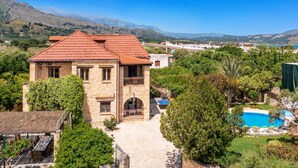 Una casa de piedra con techo rojo, piscina y vistas a las montañas.