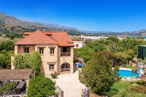 A stone house with a red roof, a swimming pool, and a view of mountains.