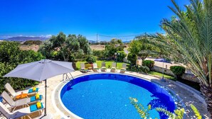 Una piscina con sillas de descanso y una sombrilla, rodeada de follaje y una vista despejada del paisaje.