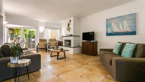 A living room with a sofa, armchairs, a TV, and a fireplace. - Villa Capri Crete by Villa Plus (Chersonisos)