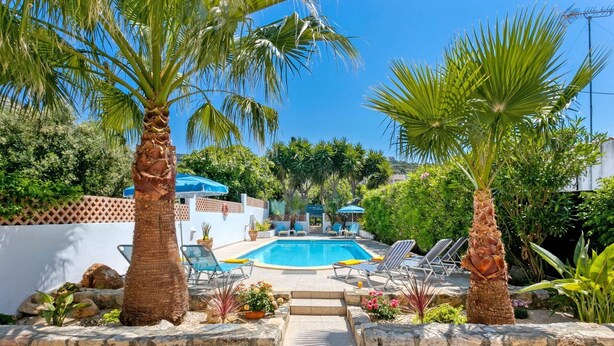 A swimming pool with lounge chairs, surrounded by palm trees and potted plants. - Villa Capri Crete by Villa Plus (Chersonisos)