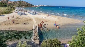 Une plage avec une eau claire et peu profonde, une promenade en bois et des parasols.