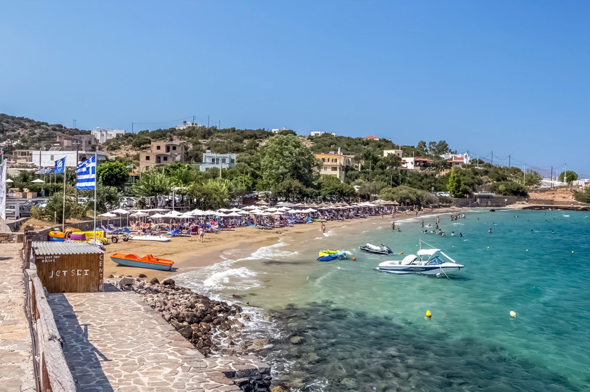 A coastal beach scene with clear waters, umbrellas, and boats.