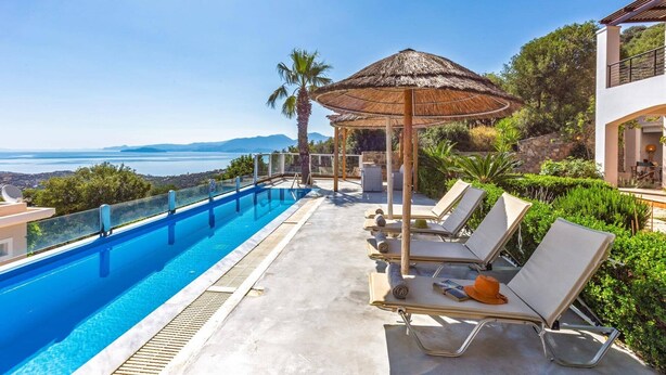 Une piscine avec des chaises longues et un parasol en chaume, offrant une vue panoramique.