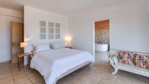 Une chambre à coucher comprenant un lit, des tables de chevet, un banc et une salle de bain avec une baignoire.