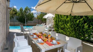 Comedor con una mesa dispuesta para el desayuno, con vista a una piscina y abundante vegetación.