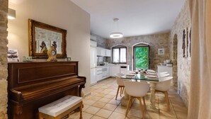 Comedor con piano, una mesa preparada para cuatro personas y vistas a una cocina y jardín a través de una puerta.