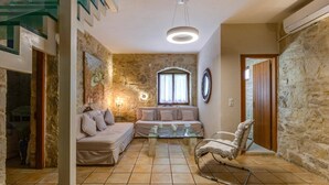 Una sala de estar acogedora con una pared de piedra, un sofá, una mesa de centro de vidrio y un sillón mecedora.