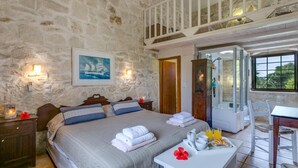 Un dormitorio con pared de piedra, una cama con toallas, un cuadro, ducha y una mesa para el desayuno.