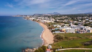 An aerial view of a coastal town with a beach, residential buildings, and a mountain in the background.