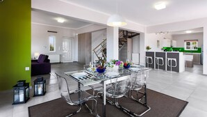 A modern kitchen with a green accent wall, a dining area with a glass table and chairs, and a staircase leading to another level. - Villa Horizon by Villa Plus (Kampani)