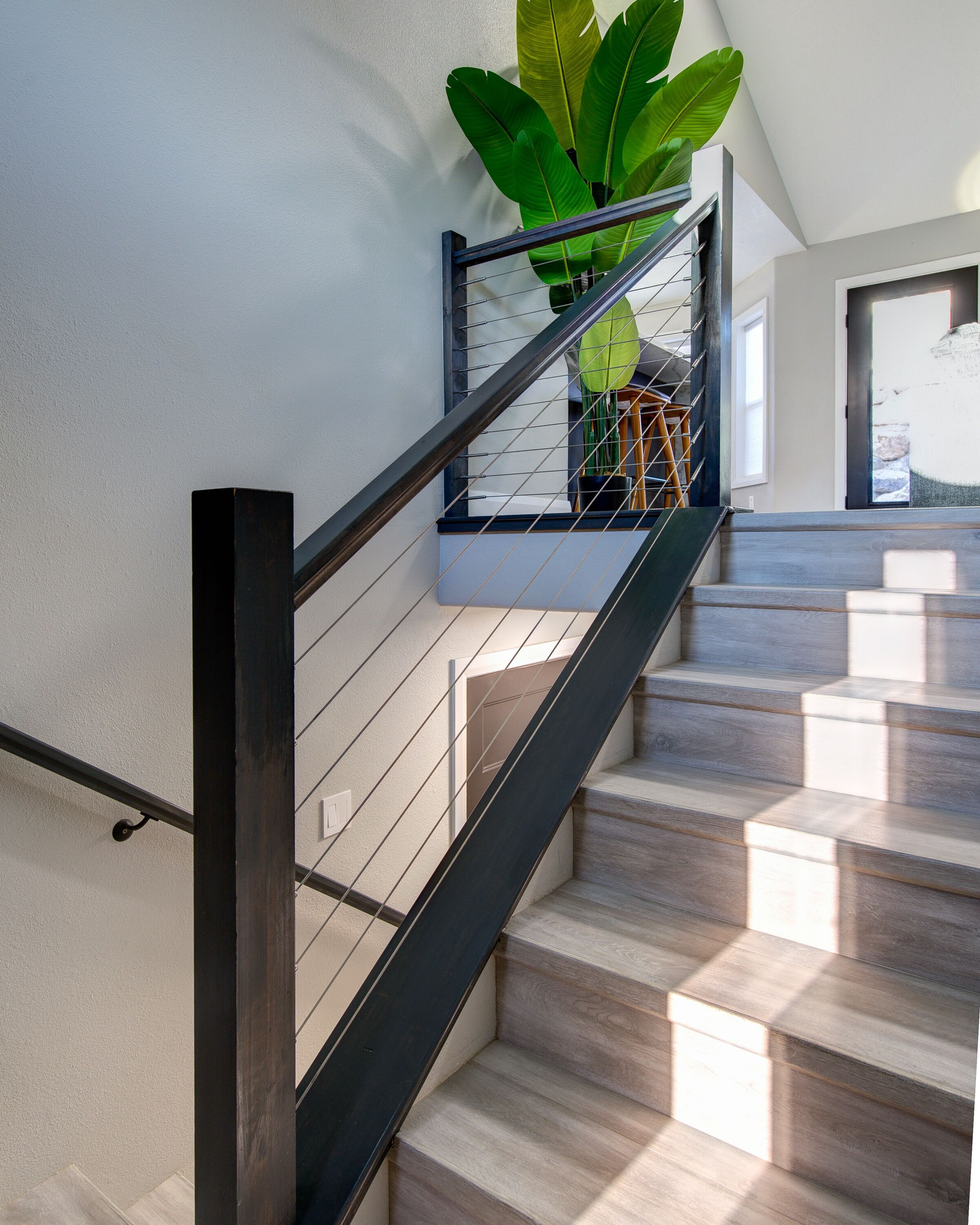 A modern staircase with wooden steps and a metal railing, leading to a landing with a large potted plant.