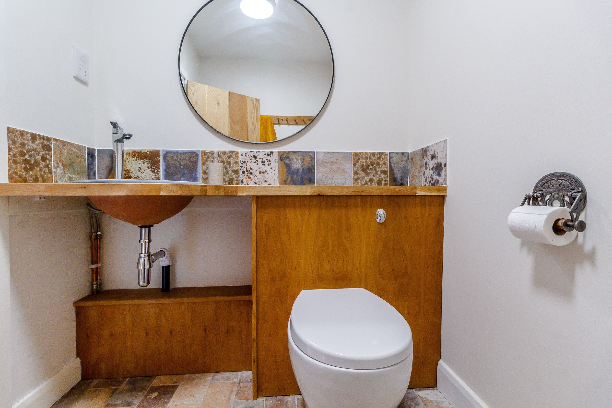 Une salle de bain avec un meuble-lavabo en bois, un miroir rond et des toilettes.