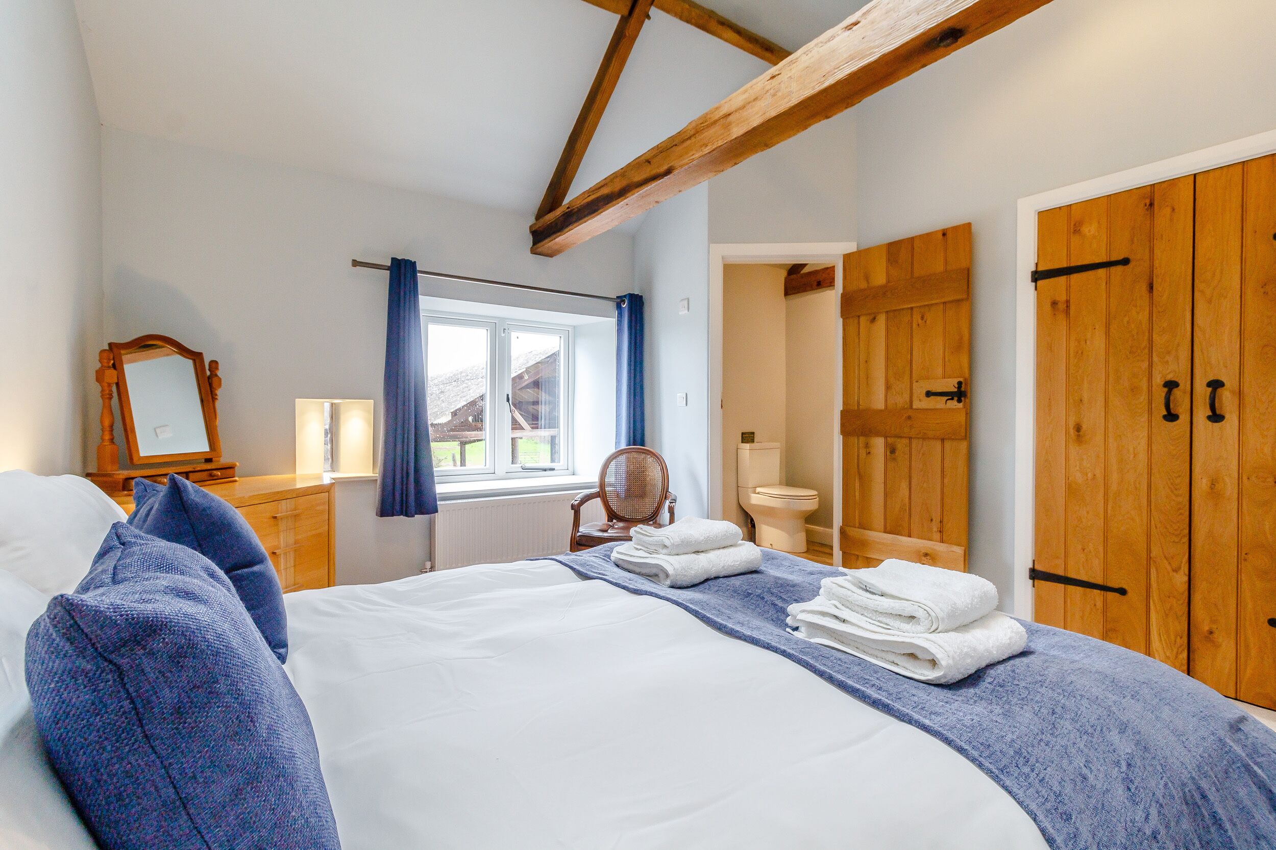 A bedroom with a large bed, wooden wardrobe, and a window with curtains.