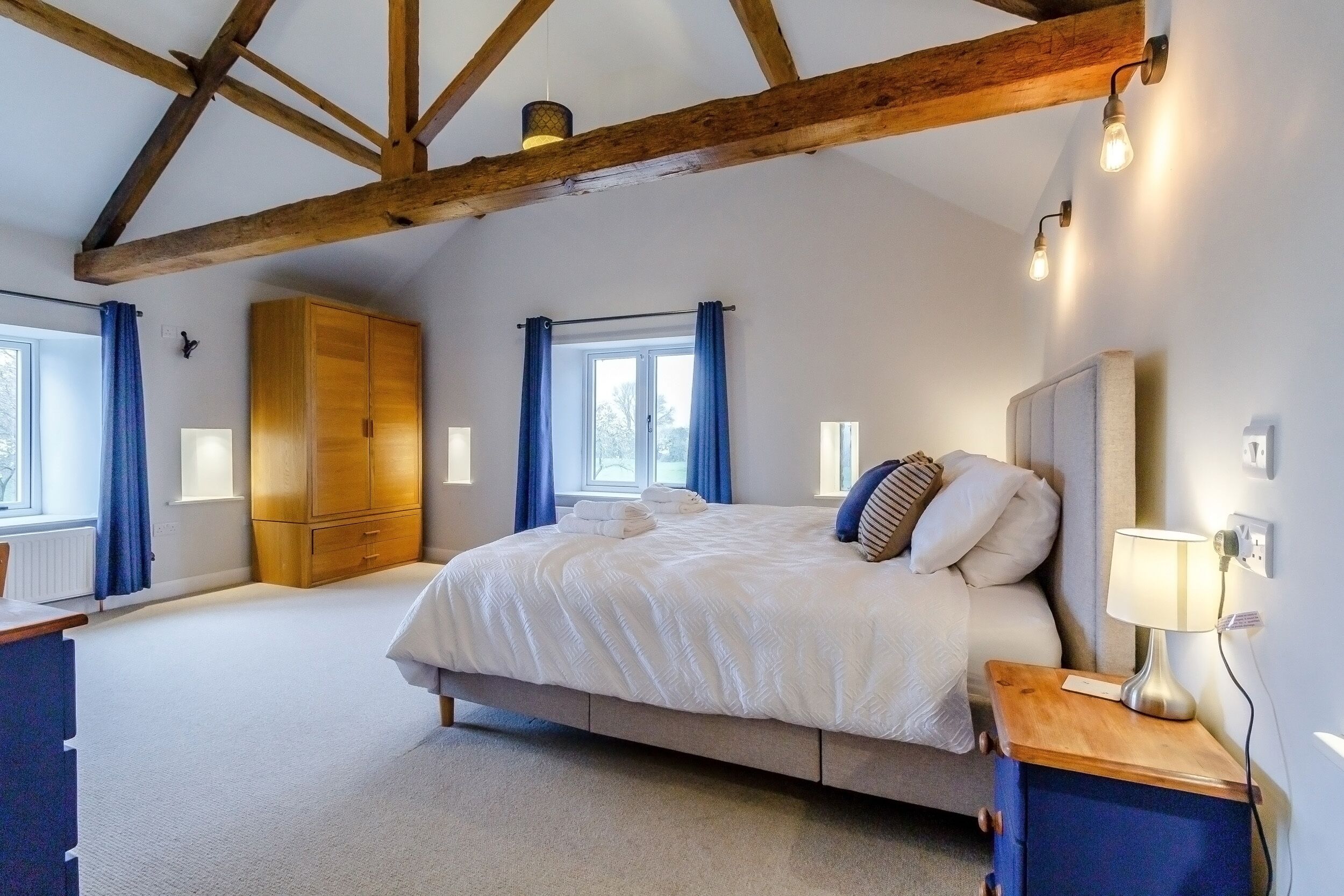 A bedroom with a large bed, wooden wardrobe, and a nightstand with a lamp.