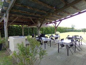 An outdoor patio with tables and chairs, a covered area with a metal roof, and a hedge in the background. - Pretty gite in the heart of the Dordogne valley sleeping 8 max (7adults) (Nadaillac de rouge)