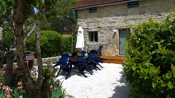 Ein Steinhaus mit Ziegeldach, einer Schotterterrasse mit blauen Stühlen und einem weißen Sonnenschirm.