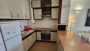 Uma cozinha compacta com armários brancos, forno embutido, micro-ondas e pia.