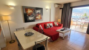 Uma sala de estar moderna com um sofá vermelho, uma mesa de jantar com cadeiras, uma mesa de centro e um grande quadro abstrato.