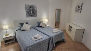 Quarto com duas camas, mesa de cabeceira com luminária, cômoda e espelho fixado na parede.