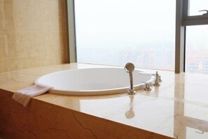 A modern bathroom with a large bathtub, a vanity with a mirror, and a view of a cityscape through large windows.