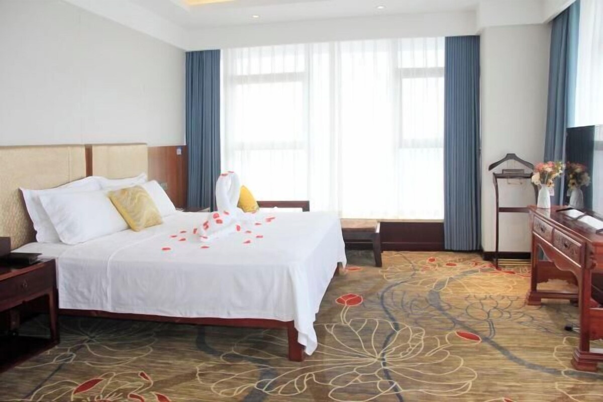 A hotel room with a bed, a nightstand, a dresser, and a window with curtains.