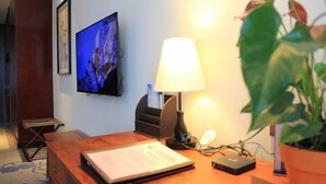 A wooden desk with a lamp, a television mounted on the wall, and a potted plant. - Lisan Garden Hotel (Ruichang)