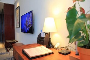 Een houten bureau met een lamp, een aan de muur bevestigde televisie en een plant in pot.
