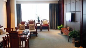 A modern hotel room with a large window, a flat-screen TV mounted on the wall, wooden furniture, and a small table with a tray. - Lisan Garden Hotel (Ruichang)