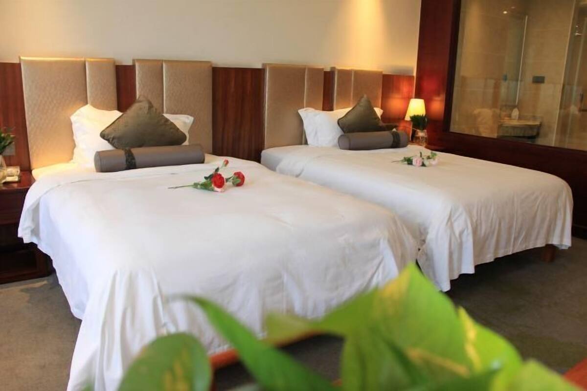 Een hotelkamer met twee bedden, elk met hoofdbord, witte beddengoed en een nachtkastje met lamp.