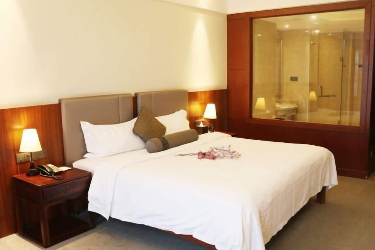 A neatly made bed with white linens, a wooden nightstand with a lamp, and a glass-enclosed shower area.