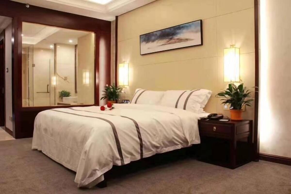 Een hotelkamer met een bed, nachtkastjes, een spiegel en een schilderij aan de muur.