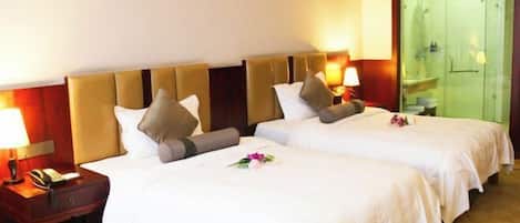 A hotel room with two beds, a nightstand with a phone, and a bathroom visible through a glass door.