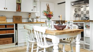 Une cuisine moderne avec des meubles blancs, une table à manger en bois et un panier de fruits.